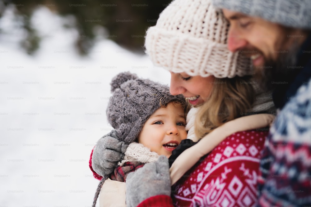 Side view of father and mother with small child in winter nature, standing in the snow.