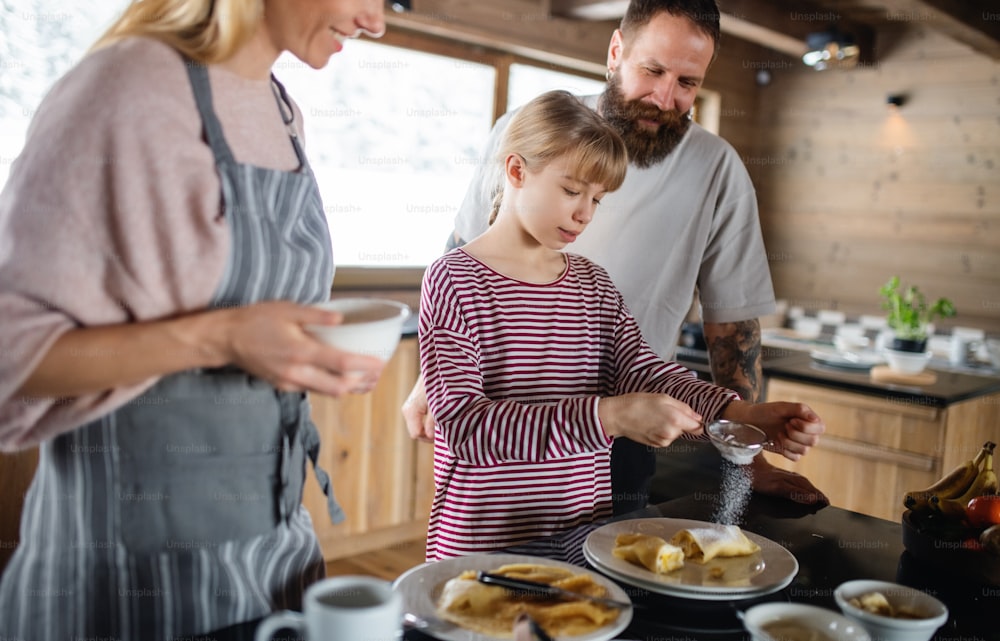 Família feliz com a filha pequena cozinhando dentro de casa, férias de inverno em apartamento privado.