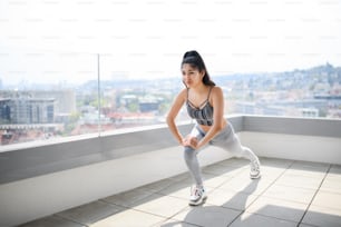 A portrait of young sport woman doing exercise on balcony outdoors in city, stretching.