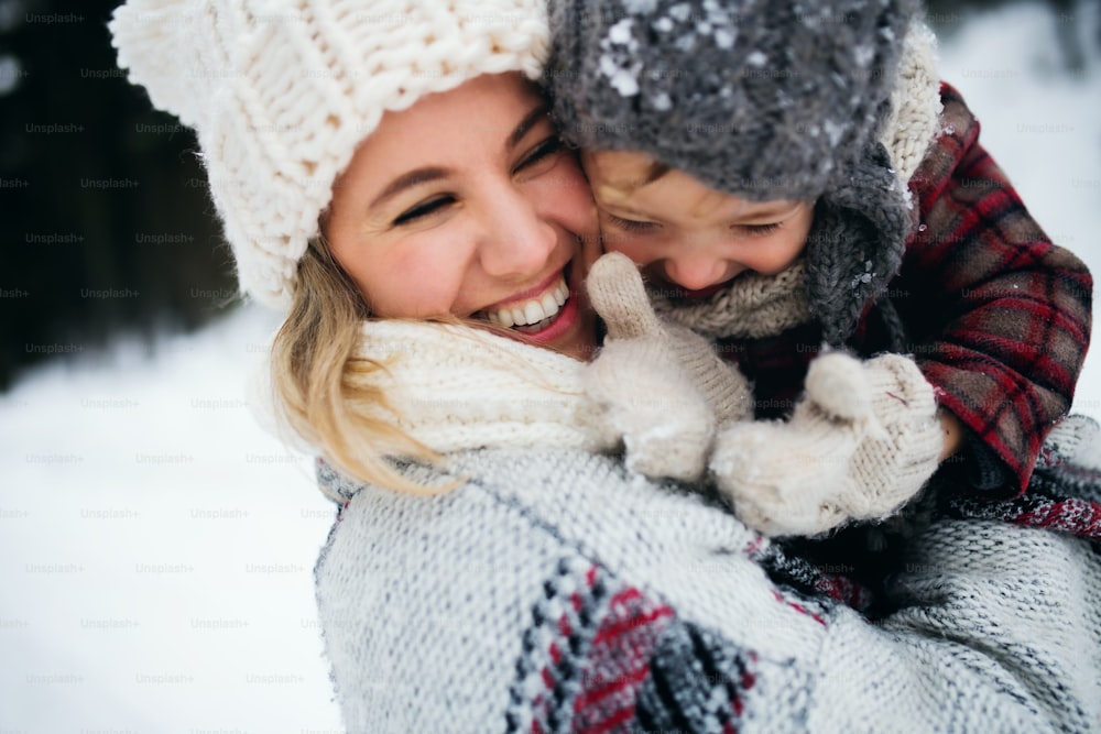 Portrait of cheerful mother with small daughter standing in winter nature, laughing.