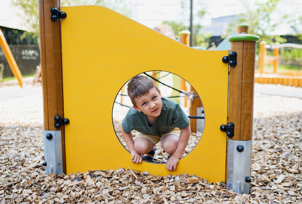 A small nursery school boy playing outdoors on playground, looking at camera