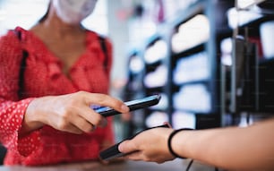 Unrecognizable woman with face mask paying by smartphone indoors in shopping center, coronavirus concept.