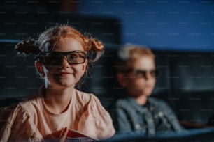 Small children with 3d glasses and popcorn in the cinema, watching film.