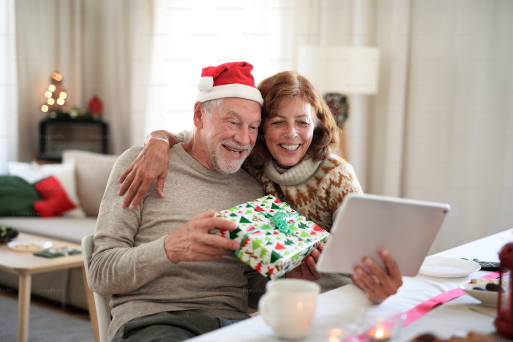 Vista frontal de una feliz pareja de ancianos en el interior de la casa en Navidad, teniendo una videollamada con la familia.