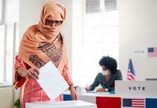 投票箱に一票を入れるイスラム女性有権者、アメリカの選挙とコロナウイルスのコンセプト。