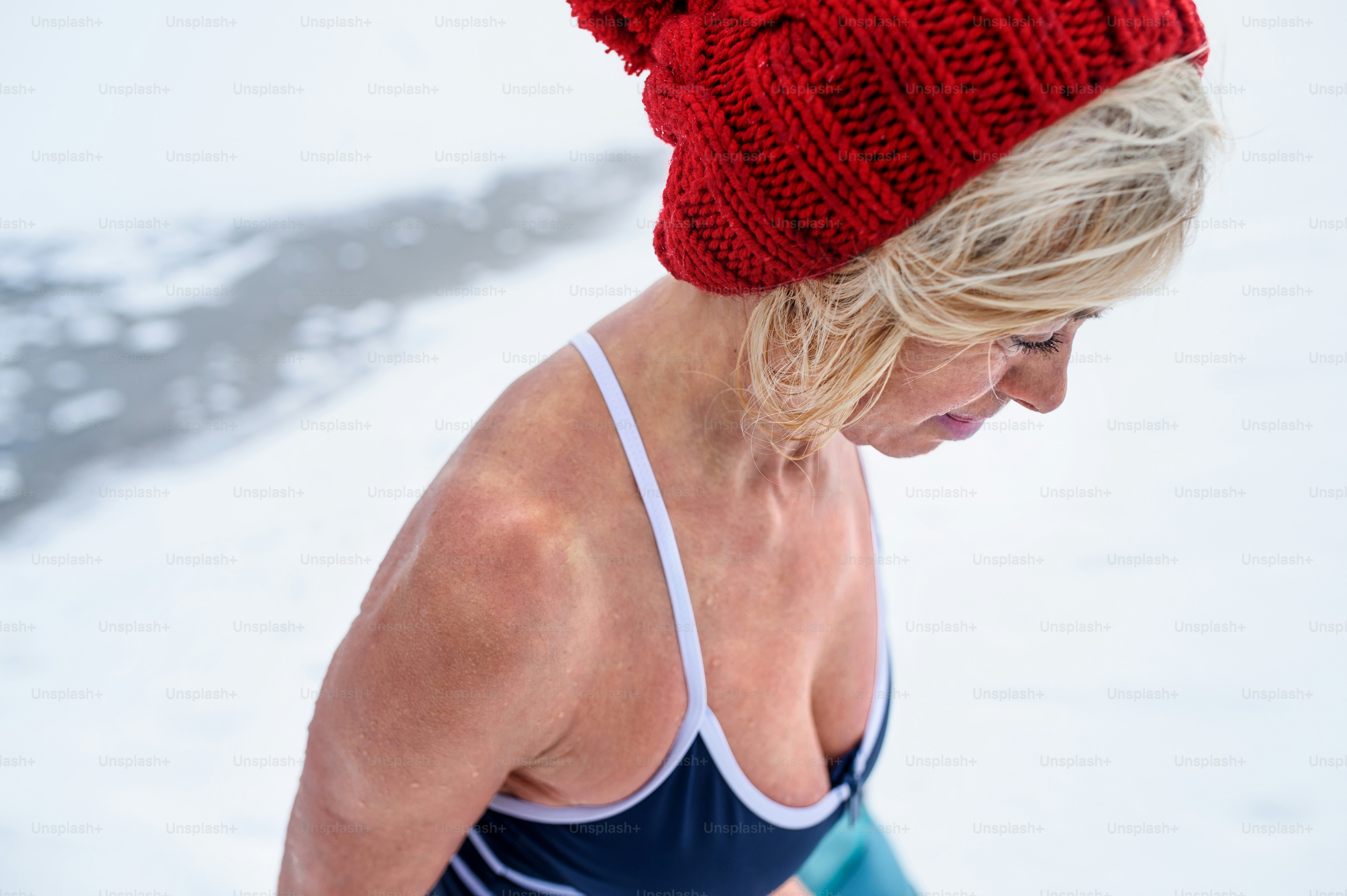 Nahaufnahme einer aktiven Seniorin im nassen Badeanzug, die im Winter nach draußen schaut, Kältetherapiekonzept.