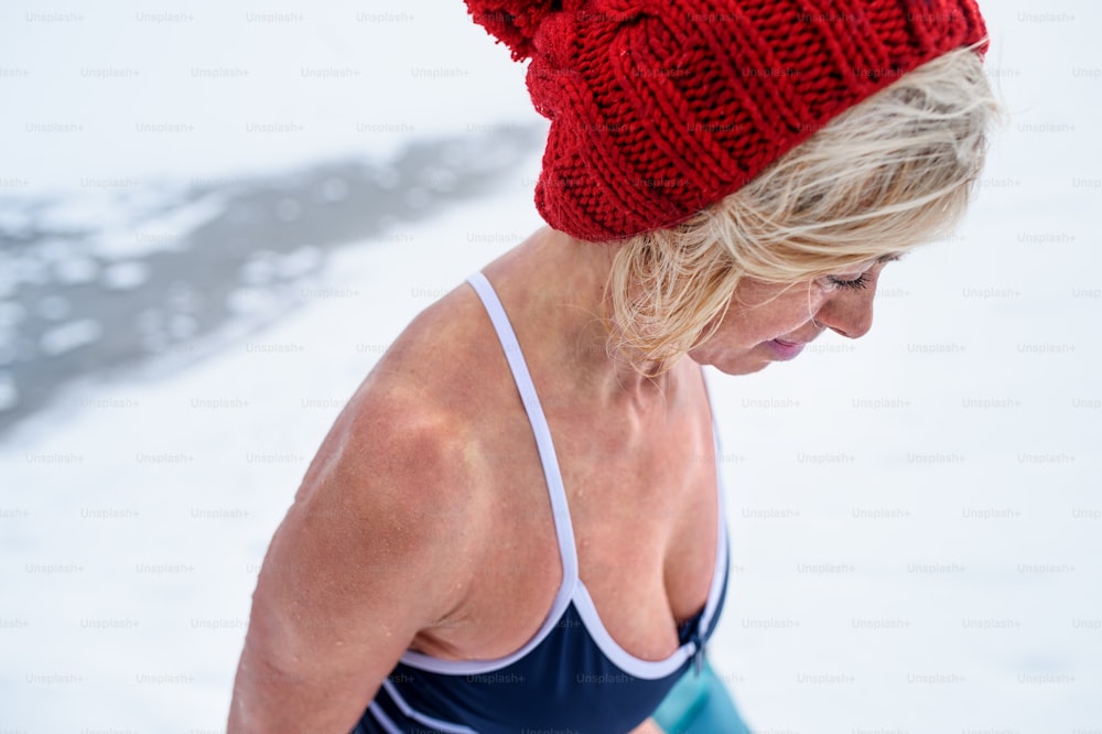 High angle view close up of an active senior woman in wet swimsuit looking down outdoors in winter, cold therapy concept.