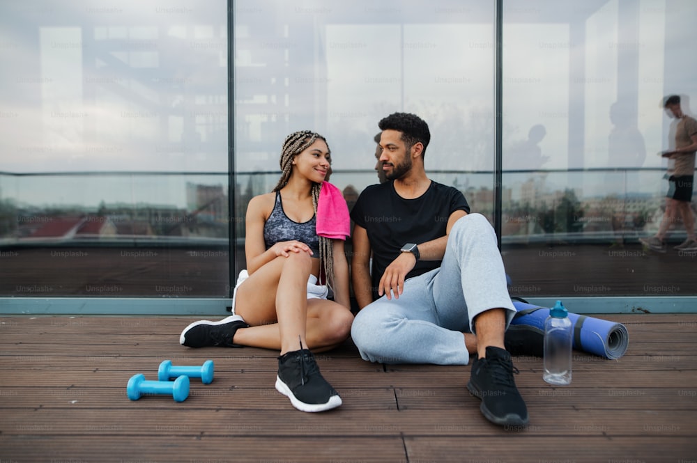 A young couple in love resting after exercise outdoors on terrace, sport and healthy lifestyle concept.