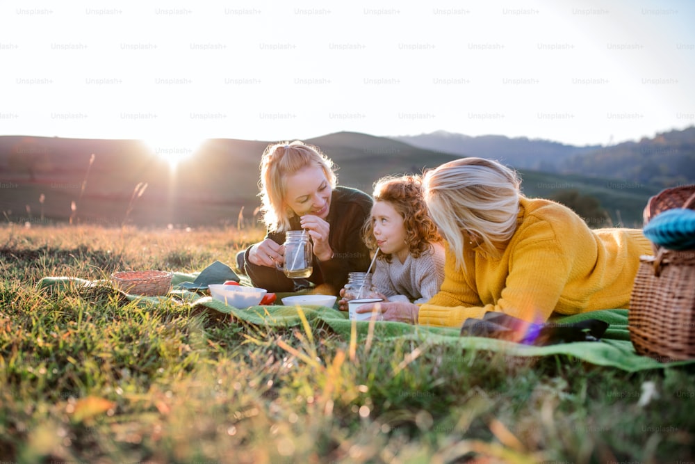 Bambina felice con la madre e la nonna che fanno picnic nella natura al tramonto.