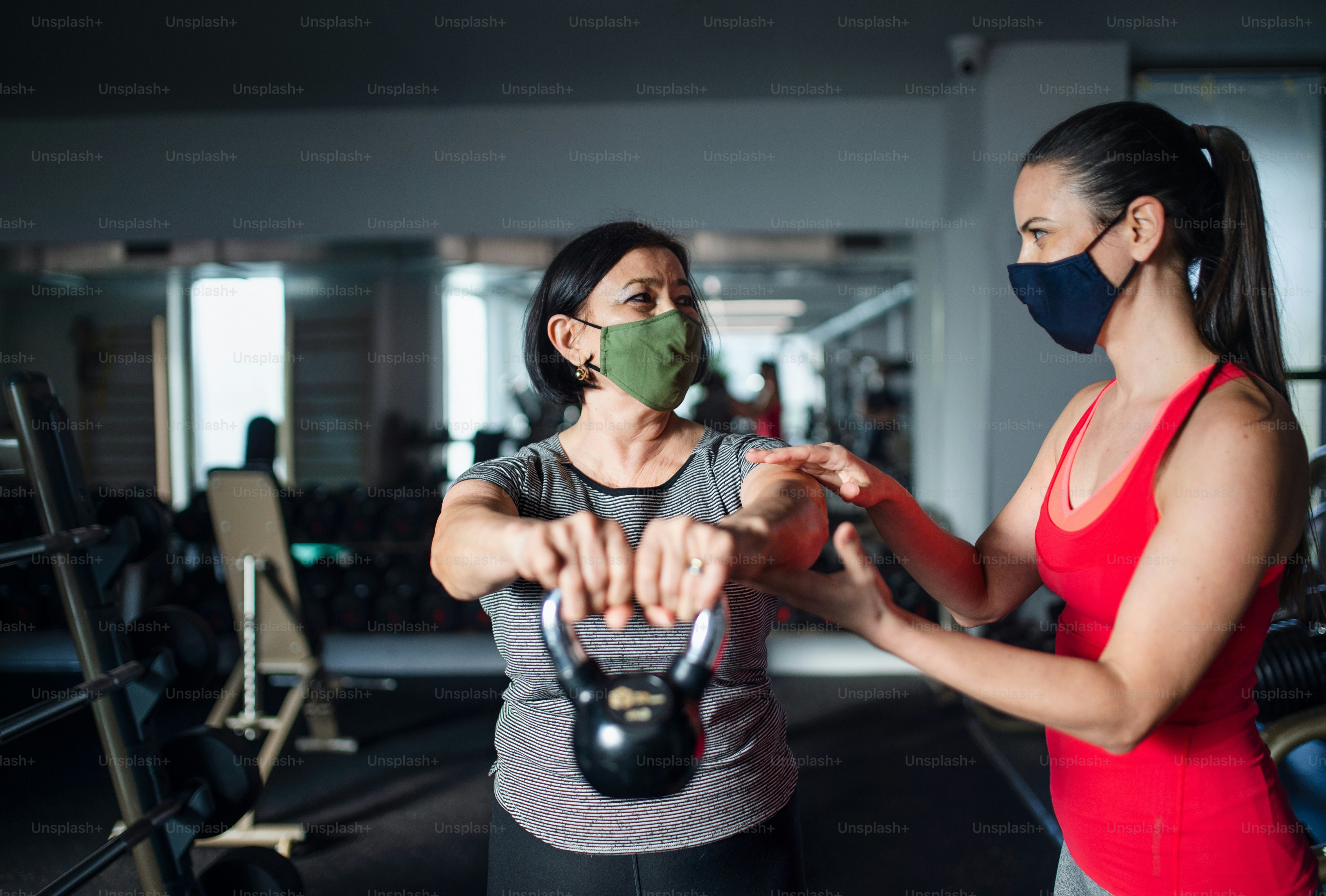 Active senior woman with personal trainer doing exercise in gym, coronavirus concept
