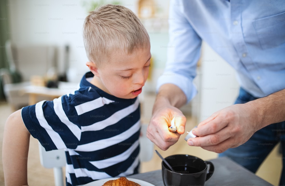 An unrecognizable father with down syndrome son indoors, lighting candle.