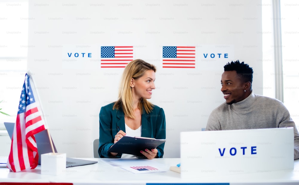 Homem e mulher membros da comissão eleitoral conversando no local de votação, eleições nos EUA.