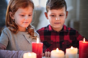 Portrait of small girl and boy indoors at home at Christmas, holding candles.