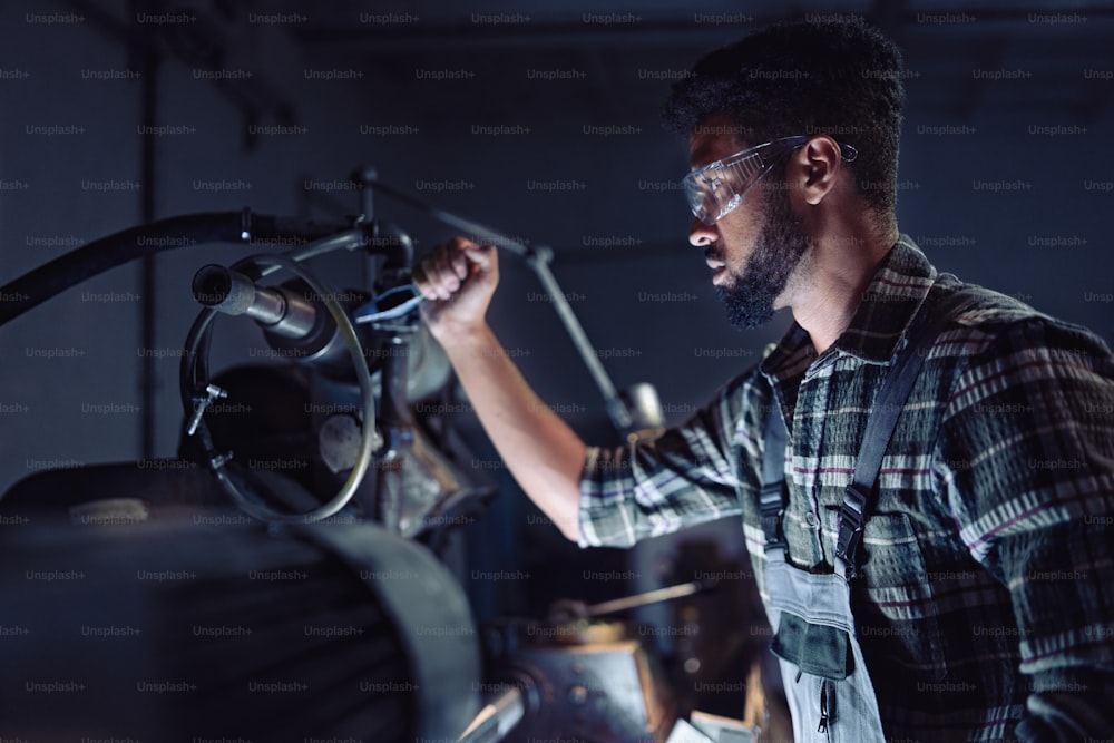 Portrait of a young concentrated african american industrial man working on cutter indoors in metal workshop.