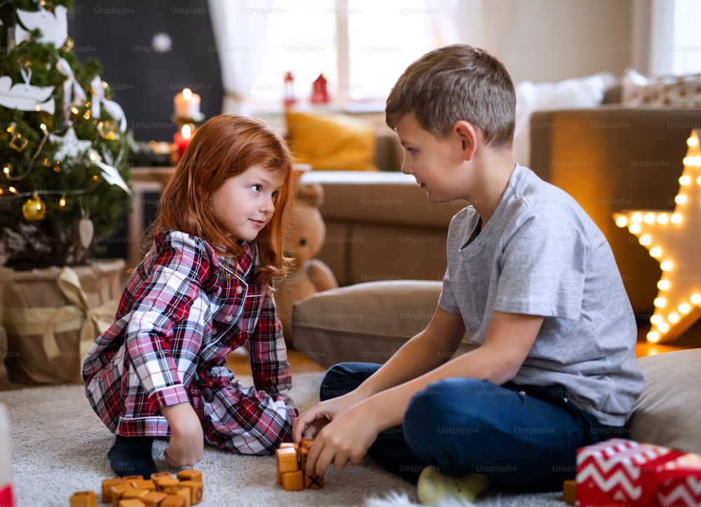 Happy small girl and boy in pajamas indoors at home at Christmas, playing board games.