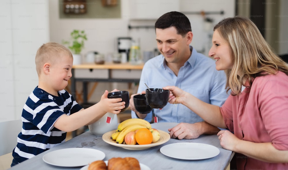 Una familia feliz con un hijo con síndrome de down en la mesa, desayunando.