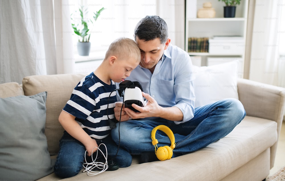 Un padre con un hijo feliz con síndrome de Down en el interior de su casa, usando gafas de realidad virtual.
