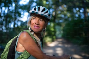 A portrait of active senior woman biker cycling outdoors in forest.