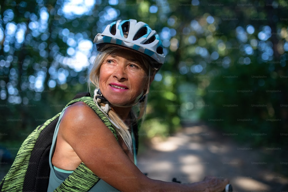 Ein Porträt einer aktiven älteren Bikerin, die draußen im Wald radelt.