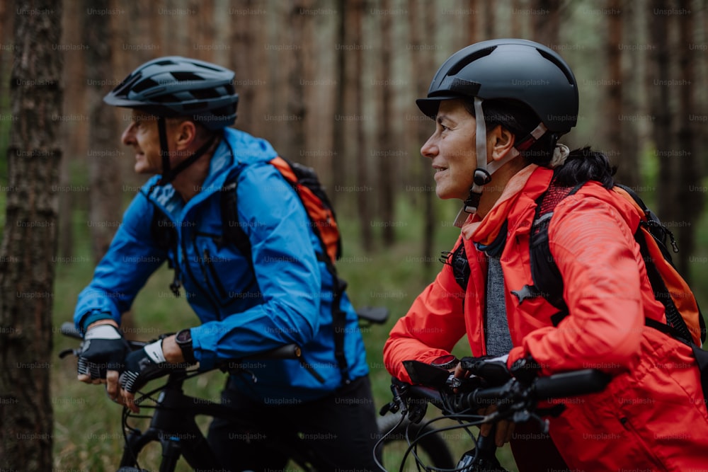 Una pareja de ciclistas mayores con bicicletas eléctricas admirando la naturaleza al aire libre en el bosque en un día de otoño.