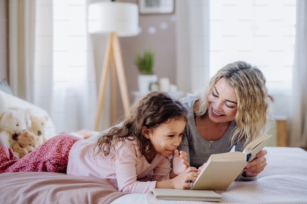 어린 딸과 함께 침대에 누워 집에서 책을 읽는 행복한 어머니.