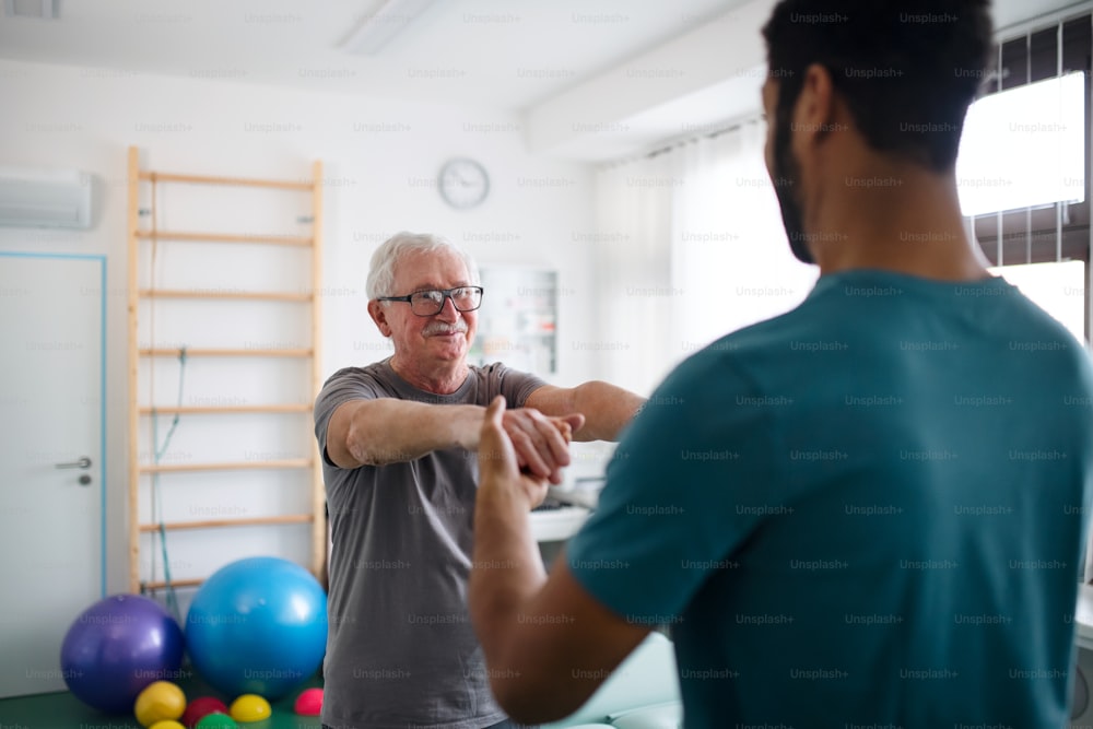 Un jeune kinésithérapeute fait de l’exercice avec un patient âgé dans une salle de physique