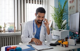 A young male doctor managing phone calls in his office.