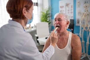 A female doctor checking senior's man throat in her office.