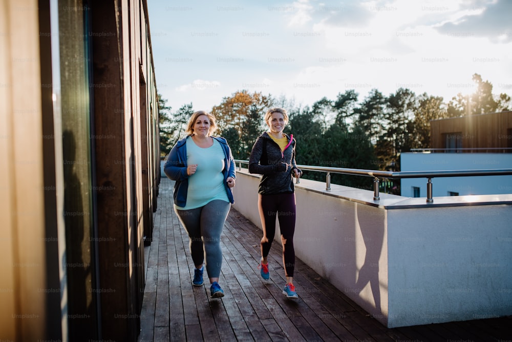 Una mujer con sobrepeso corriendo y haciendo ejercicio con un entrenador personal al aire libre en la terraza del gimnasio.