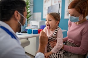 Un medico zoung che controlla la gola di una bambina nel suo ufficio.