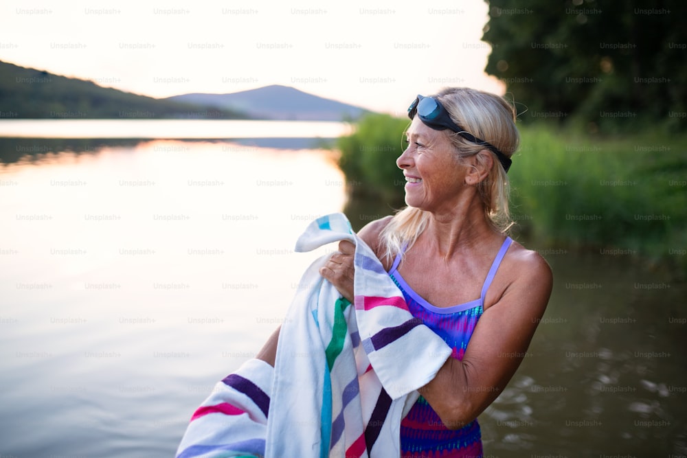 Un retrato de una mujer mayor activa nadando secándose con towell al aire libre junto al lago.