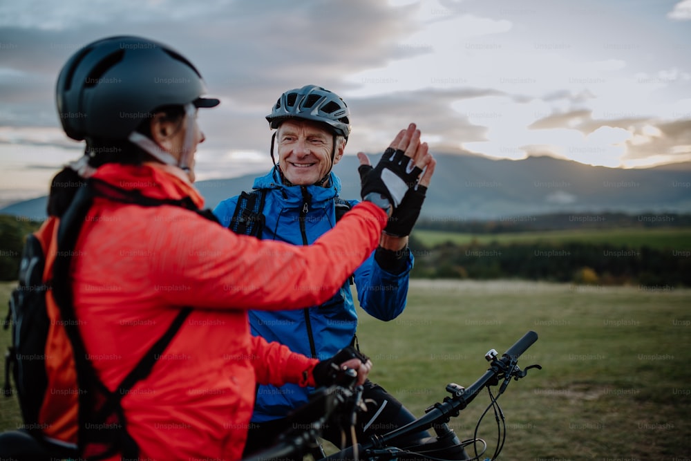 A senior couple bikers high fiving outdoors in nature in autumn day.