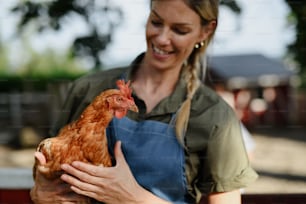 A cheerful farmer woman holding hen outdoors at farm.