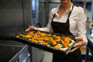 A cut out of unrecognizable female cook holding tray with baked pumpkin pieces in commercial kitchen.