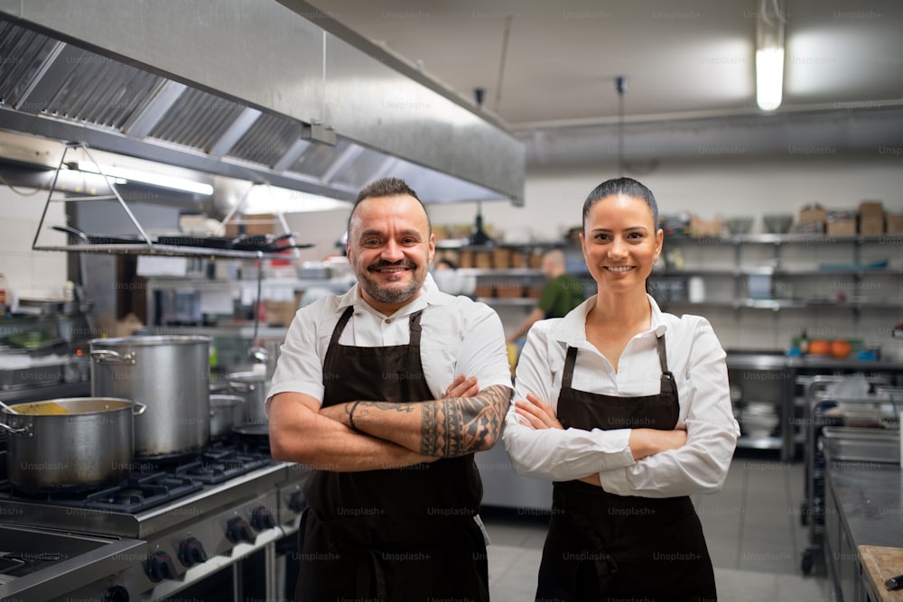 A confident chef and cook standing with arms crossed and looking at camera in commercial kitchen.