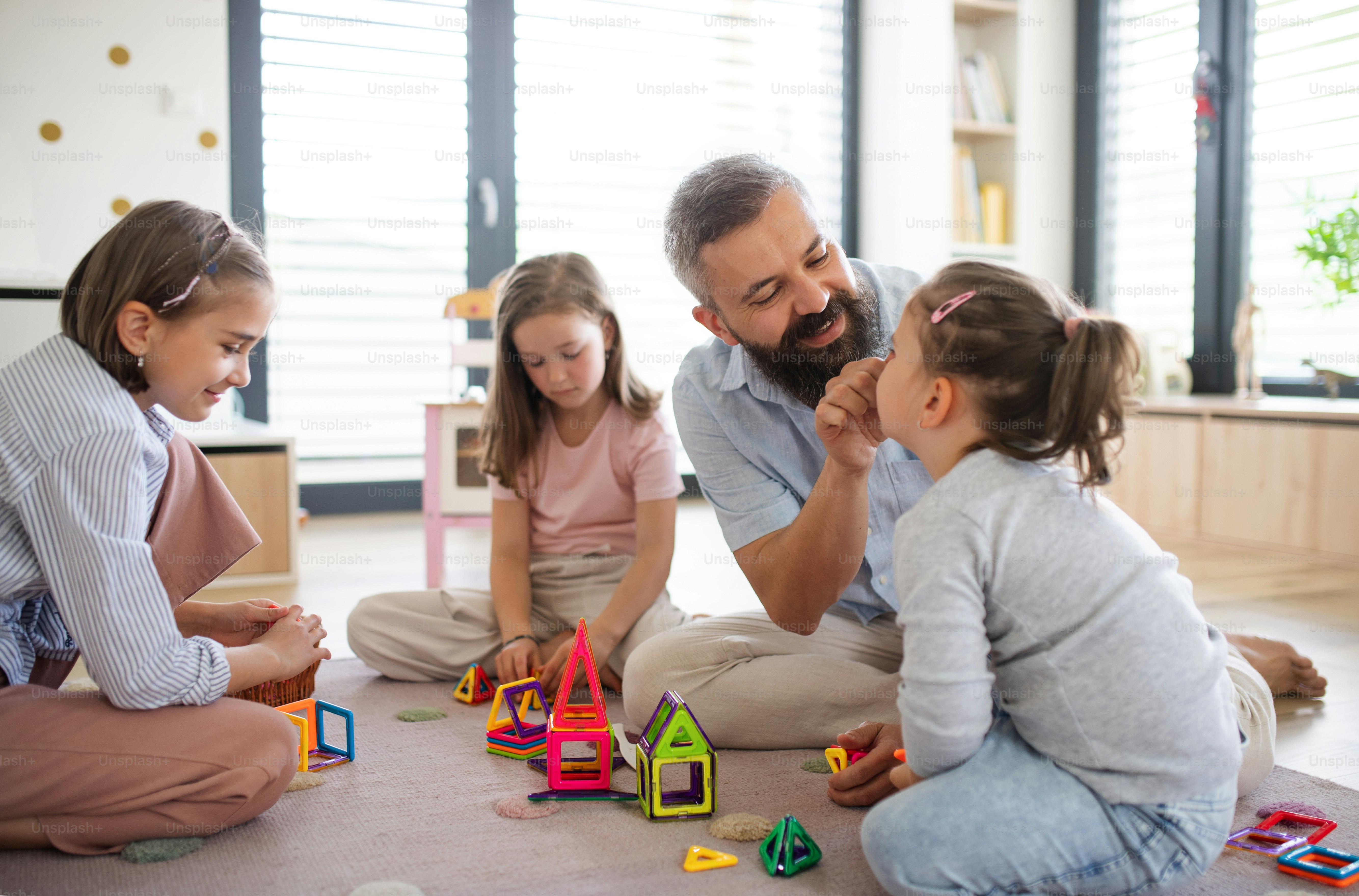 A father with three daughters indoors at home, playing on floor