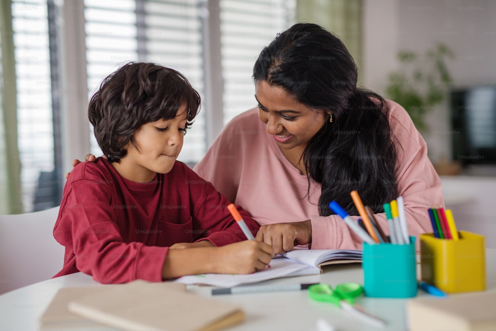 A little multiracial boy doing homework with his mother at home.