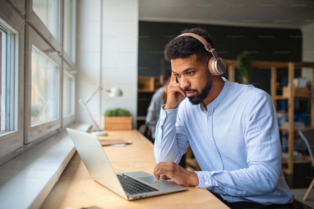 A young African-american teacher with headset and laptop indoors in staffroom.