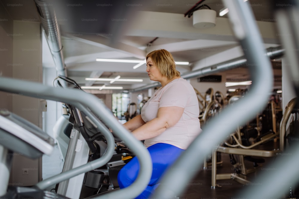 A happy mid adult overweight woman exercising on stepper indoors in gym