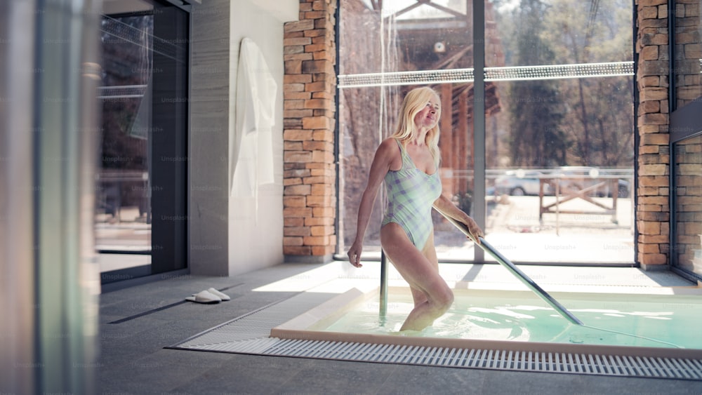 실내 수영장에서 걷고 있는 고위 여성, 건강한 라이프스타일 개념.
