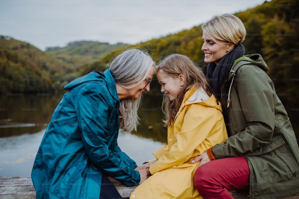 Une petite fille avec sa mère et sa grand-mère assise sur un banc et s’amusant au bord du lac.
