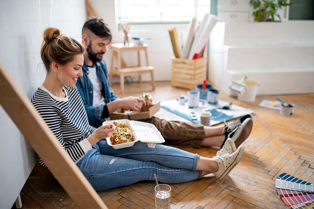ミッドアダルトカップルは、自宅で屋内で昼食を食べ、移転、DIY、フードデリバリーのコンセプト。
