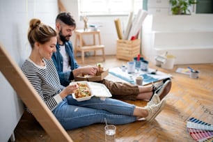 Mid adults couple eating lunch indoors at home, relocation, diy and food delivery concept.