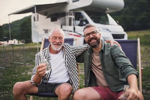 Ein reifer Mann mit älterem Vater schaut in die Kamera auf dem Campingplatz im Freien, Grillen auf Wohnwagenurlaub.