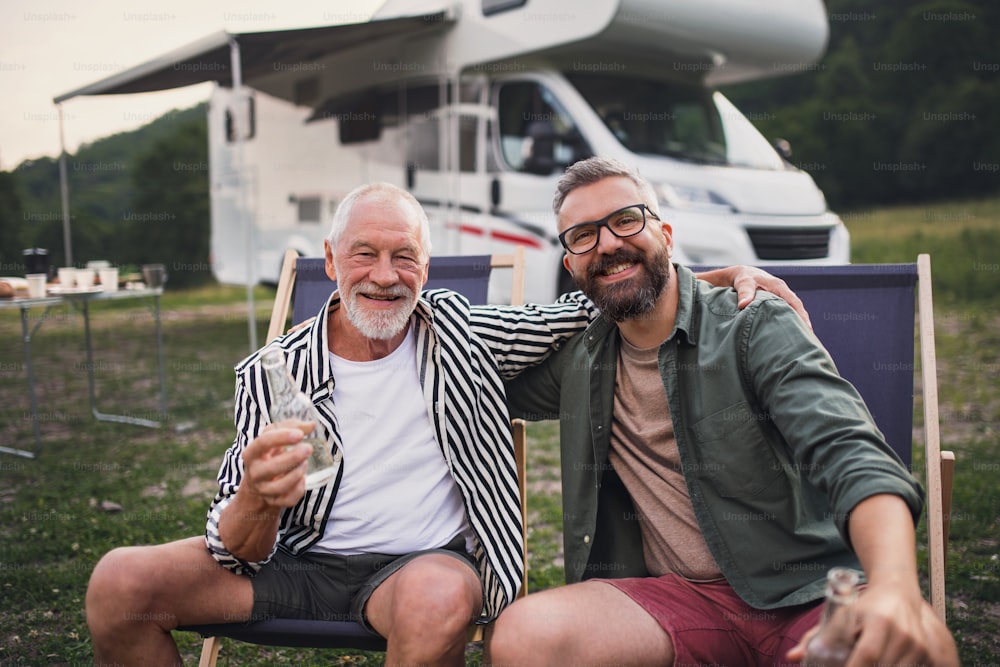 Un homme mûr avec un père âgé regardant la caméra au camping en plein air, barbecue lors d’un voyage de vacances en caravane.