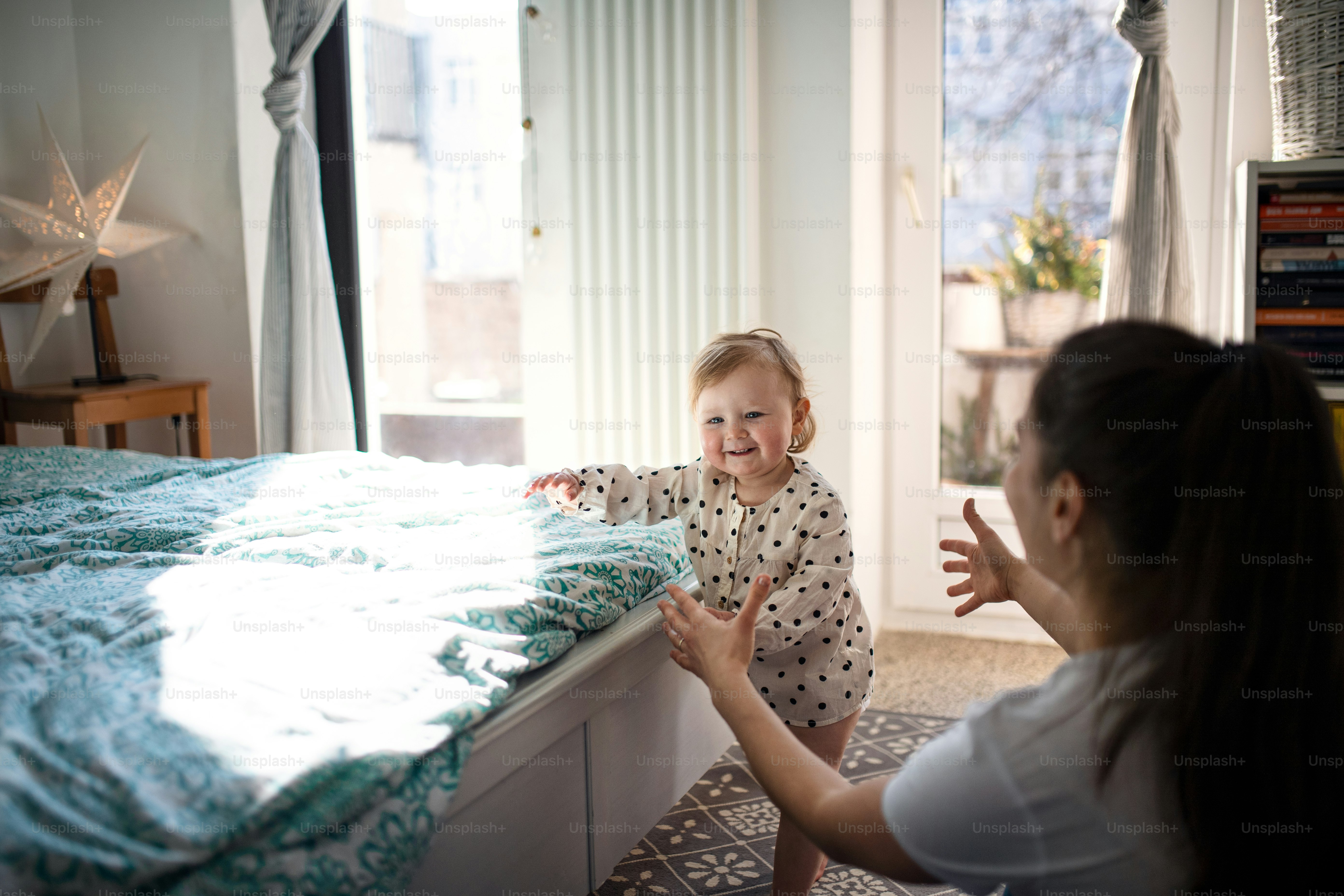 Uma menina pequena com a mãe aprendendo a andar no quarto em casa, primeiros passos conceito.