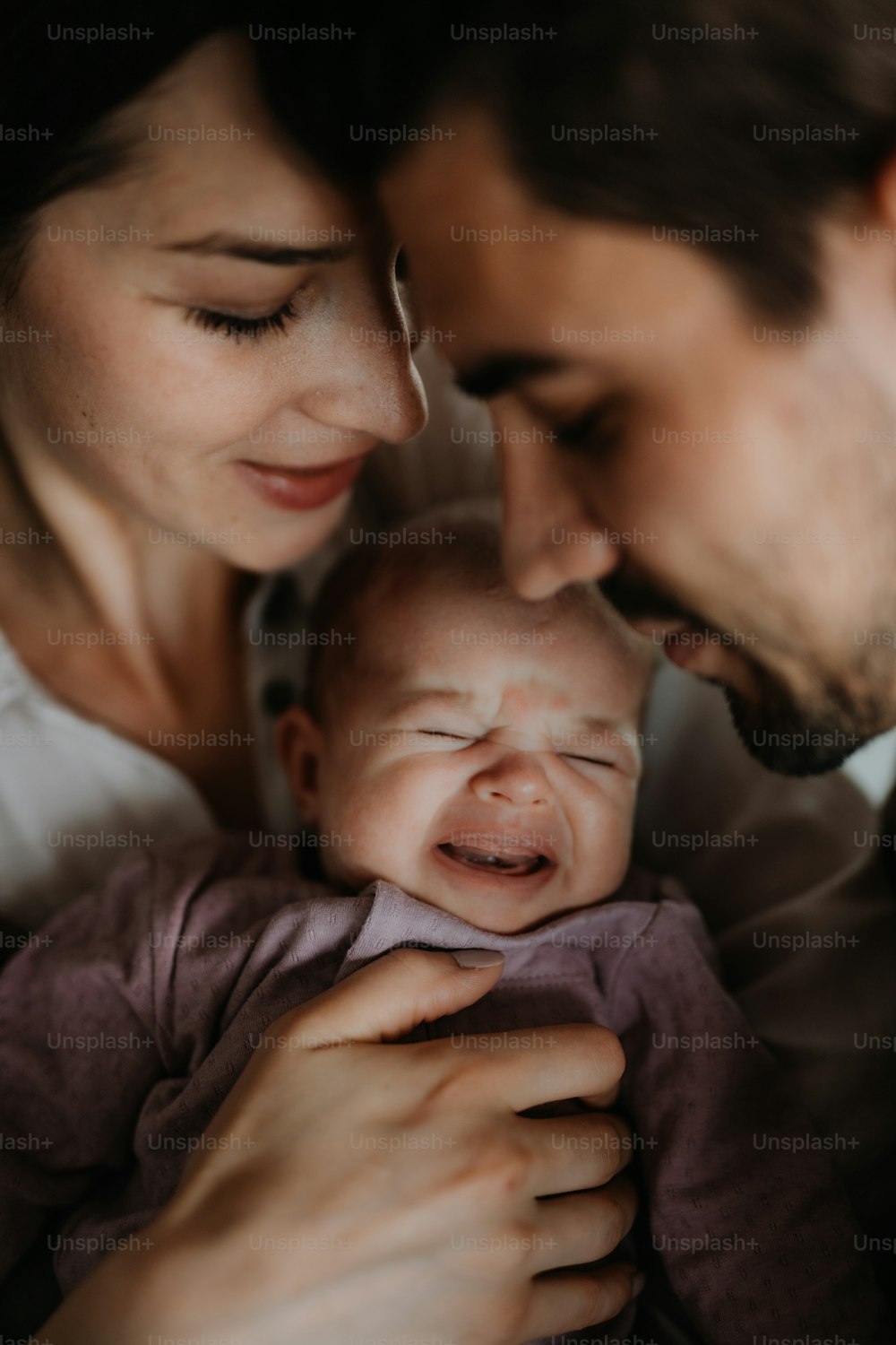 Close up of happy young parents holding and kissing their newborn baby indoors at home