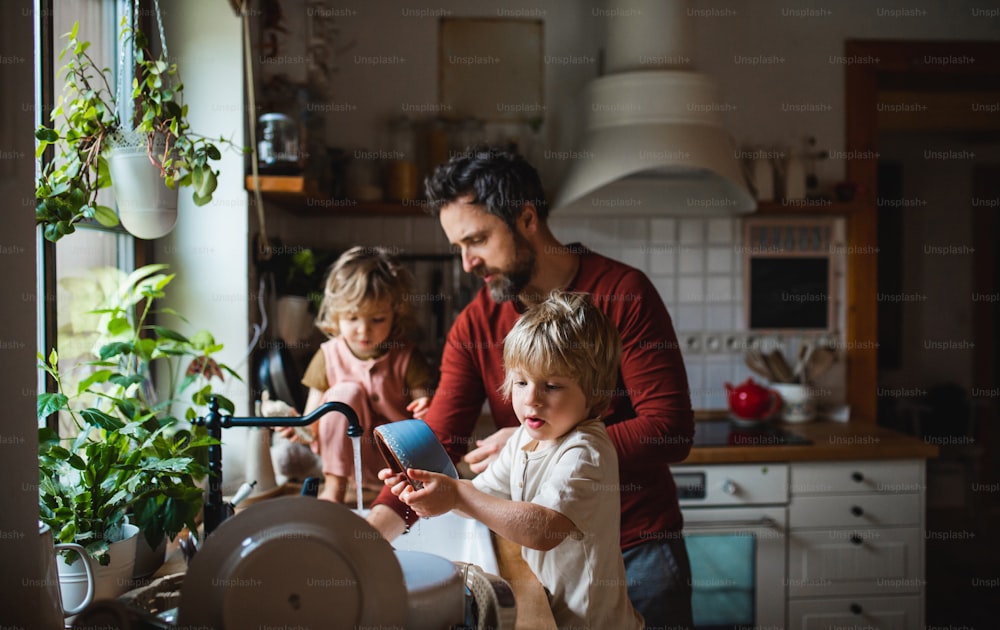 A mature father with two small children washing dishes indoors at home, daily chores concept.
