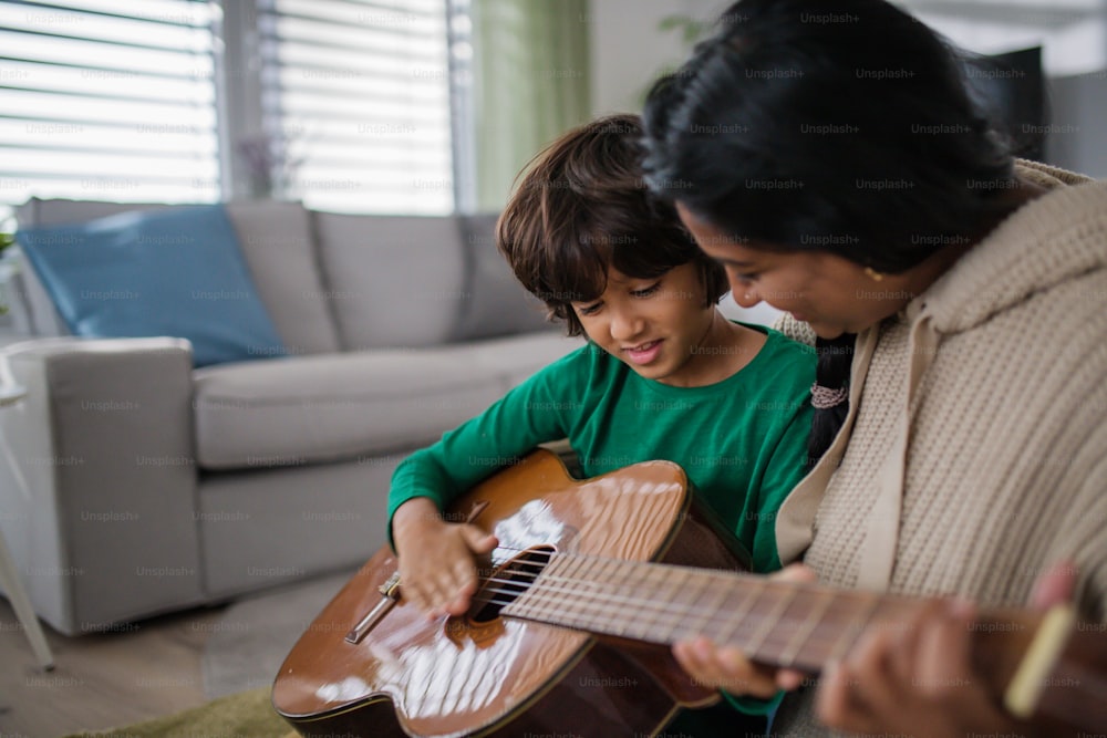 家で母親と一緒にギターを弾くことを学んでいる小さな多民族の少年。