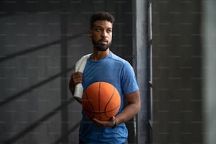 A young African American basketball player standing indoors at gym.